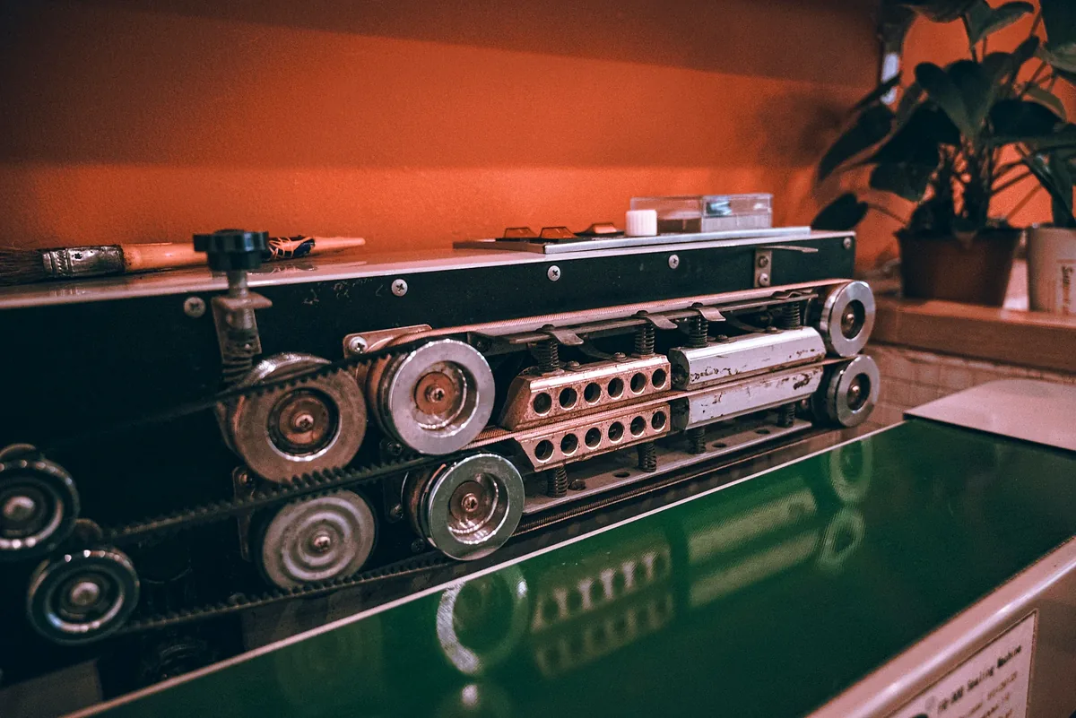 Exposed rollers and drive belts above a green conveyor belt.