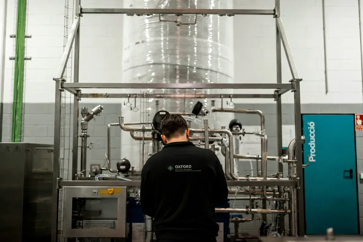 Person facing industrial pipework and a metal frame.
