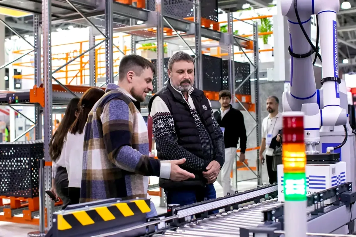 People beside a robot arm and roller conveyor.